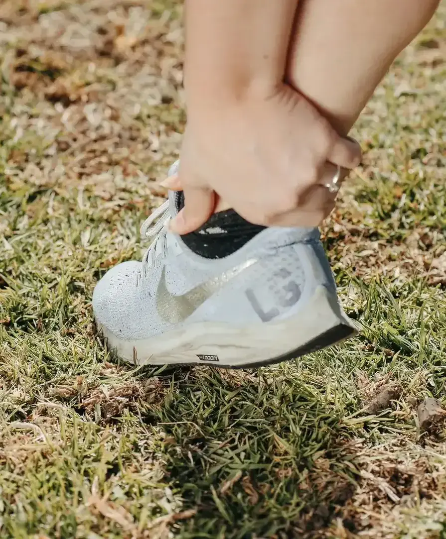close up of a women's lower leg wearing running shoe holding her ankle in pain