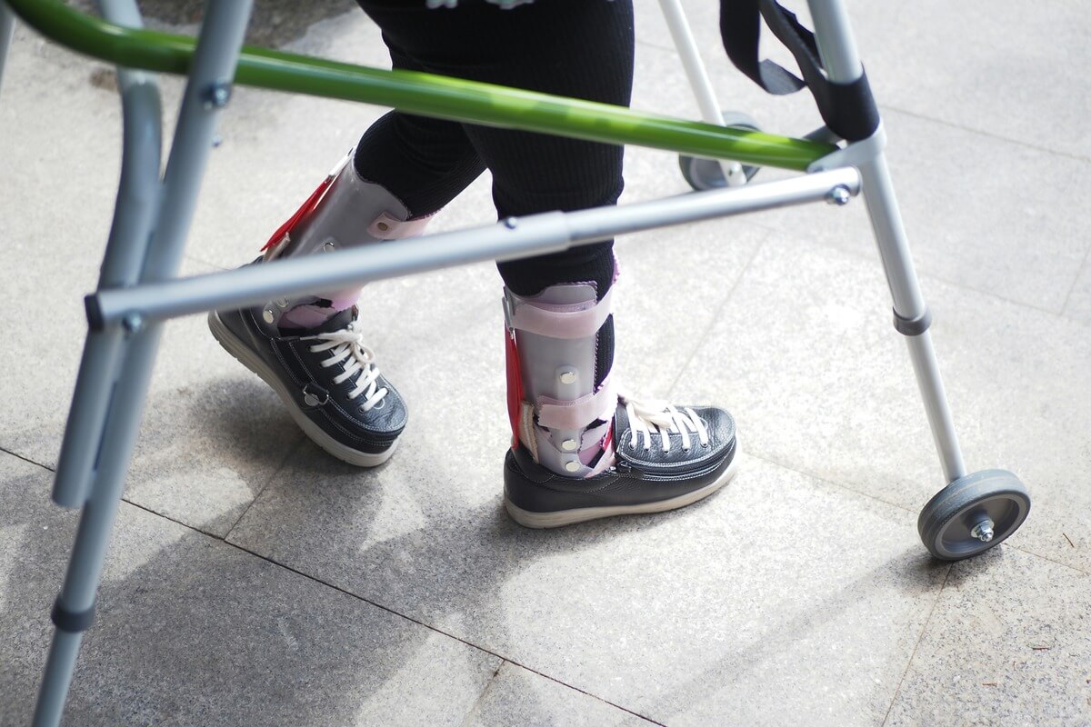 Person using a walker to assist in walking with two ankle braces on